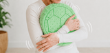 Person holding a green cushion and sitting on a blue cushion with a visible brand logo.